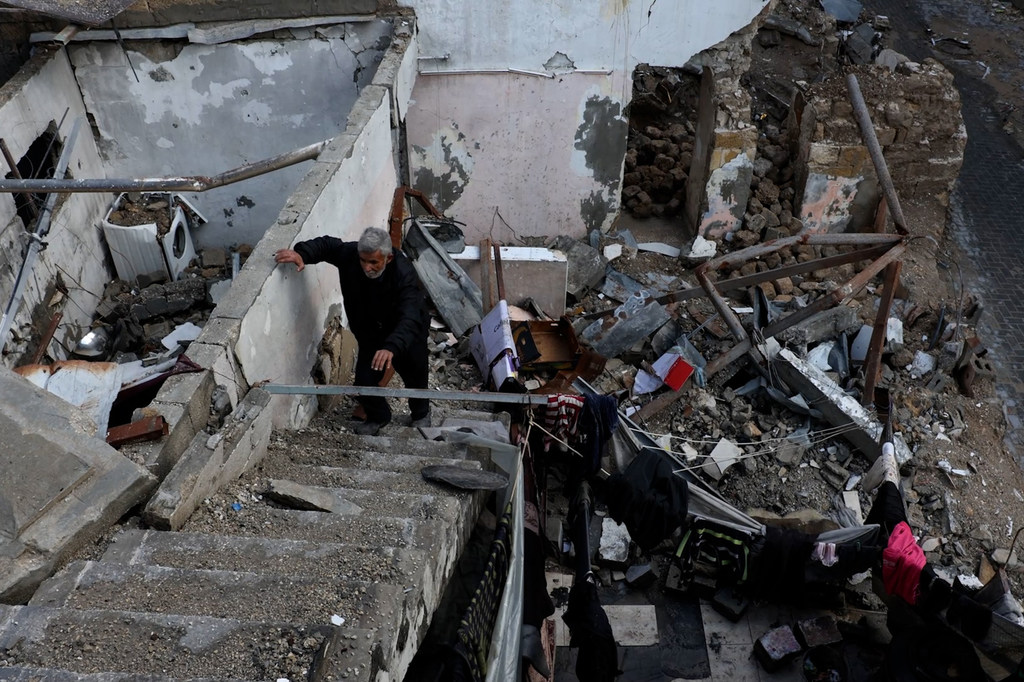 رجل يصعد إلى بقايا منزله المتضرر في غزة، في مشهد يعكس خطورة الأوضاع المعيشية التي يواجهها المدنيون.